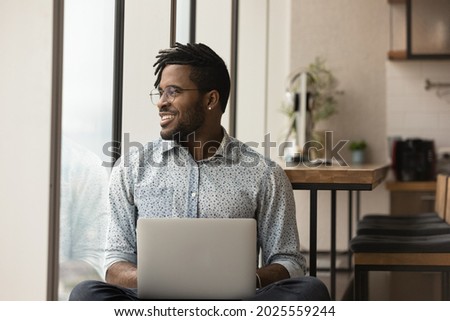 Distracted from laptop work African hipster guy looks into distance smile feel satisfied by career in company sit near window admires view. Business vision, opportunity, modern tech, lifestyle concept Royalty-Free Stock Photo #2025559244