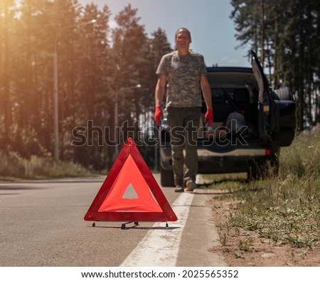 Triangle caution sign on road near broken car withdriver walking toward it.