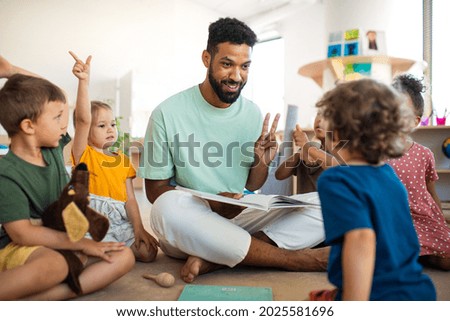 Group of small nursery school children with man teacher sitting on floor indoors in classroom, having lesson. Royalty-Free Stock Photo #2025581696