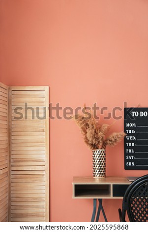 Comfortable workplace with folding screen near color wall in room