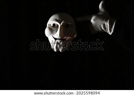 White scary mask on a black background with whites hands.