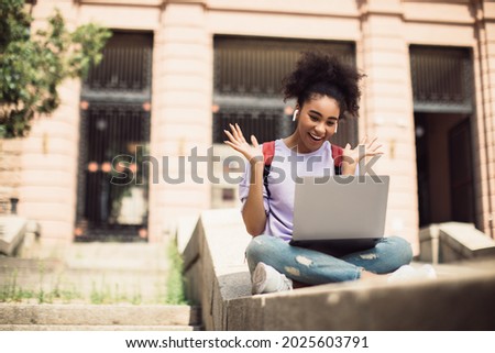 Remote Education. Black Student Girl Video Calling Via Laptop Having Online Lecture Sitting Near University Building Outdoors. Young Female Wearing Earbuds Talking To Computer Webcam. E-Learning Royalty-Free Stock Photo #2025603791