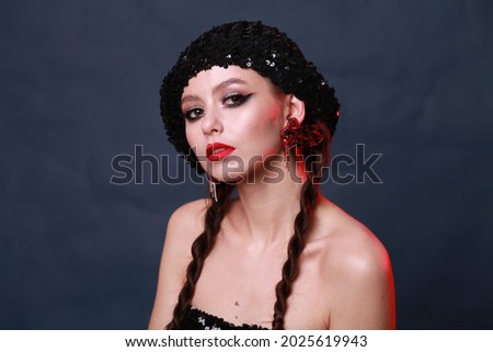 Natural female beauty concept. Emotive portrait of a fashionable model with braids and bright make-up with red lipstick. Perfect skin. Close up. Studio shot over dark background with red mixed light
