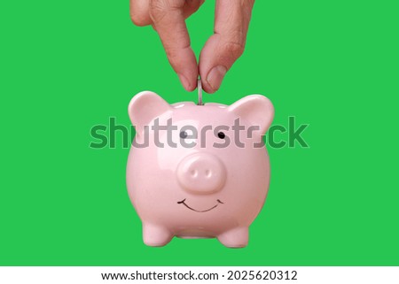 Hand is putting a coin or money in a piggy bank on chroma key green screen background. Saving money concept.