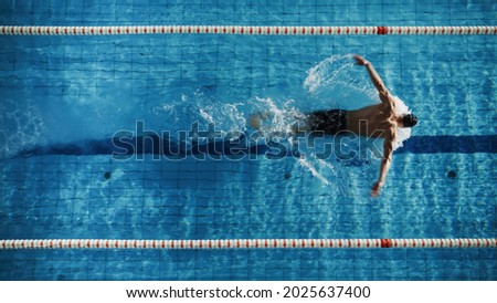 Aerial Top View Male Swimmer Swimming in Swimming Pool. Professional Determined Athlete Training for the Championship, using Butterfly Technique. Top View Shot Royalty-Free Stock Photo #2025637400