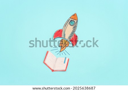 Painted rocket and open notebook over pastel blue background