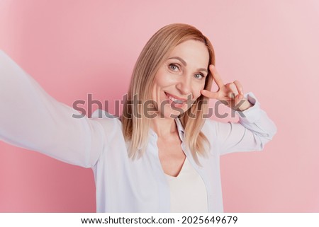 Attractive young woman happy positive smile shows peace v-sign sign make selfie on isolated pink background