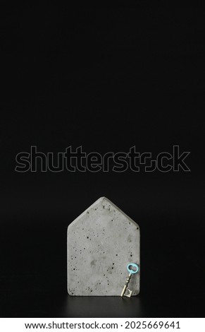 Mini concrete house model and a key on the black background. Buy a house. Concept for property ladder, mortgage and real estate investment. Free space for text, copy space, modern layout.