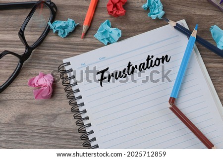 Message on FRUSTRATION written on the notebook with broken pencil, crumpled papers and eyeglasses on the wooden background.  Noise is visible due to the texture of the subjects