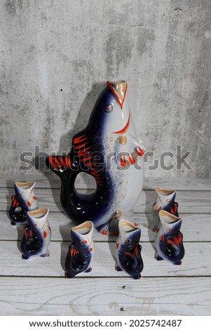 A set of a jug and glasses in the form of large and small fish. Photo on a light background.