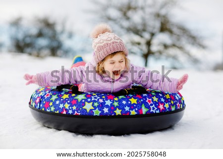Active toddler girl sliding down the hill on snow tube. Cute little happy child having fun outdoors in winter on sledge . Healthy excited kid tubing snowy downhill, family winter time.