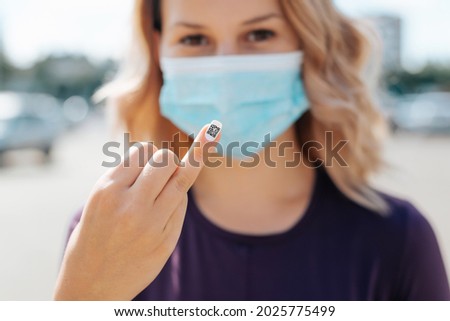Close-up of young woman in medical face mask shows qr code manicure on finger on street outside, confirmation of coronavirus vaccination. New normal concept, pass by qr code.