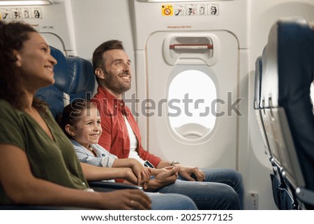 Happy caucasian family, parents with little daughter smiling and holding hands together while sitting on the airplane. Transportation, vacation concept Royalty-Free Stock Photo #2025777125