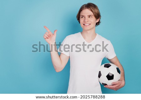 Photo of cheerful man point finger empty space holding soccer ball isolated blue background