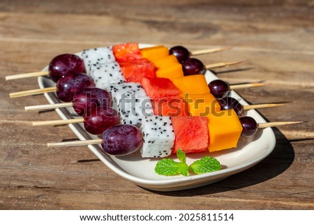 Fresh tropical fruit - grapes, mango, watermelon and pitahaya on skewers in white plate - healthy breakfast, weight loss concept. Thailand. Close up