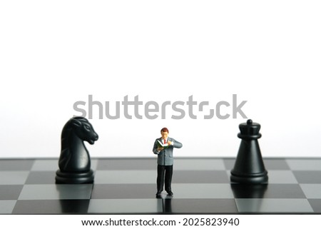Miniature people toy figure photography. Defensive or attack strategies concept. A men student standing in between horse and castle chessboard pawn knight, isolated on white background. Image photo