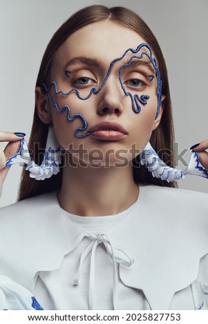 Portrait of woman in blue wire mask and with blue and white fish earrings. Creative accessories on marine theme                               