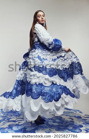 Woman in long wonderful dress with blue and white waves. Drawing and ruffles on clothes. Model standing on the blue waves drawing                                