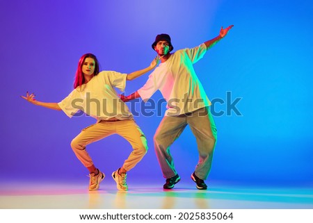Knee movements. Two young people, guy and girl, dancing contemporary dance, hip-hop over blue background in neon light. Modern dance aesthetics concept. Copyspace for ad. Royalty-Free Stock Photo #2025835064