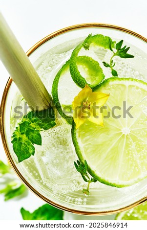 Close-up of the top of a glass with a garnishing of fresh flowers, lime slices inside summer detox refreshing drinks mocktail. Cold summer lemonade. macro.