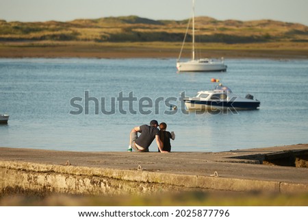 Young couple on honeymoon. Lovers sitting on the pier and looking at sea. Romantic silhouettes of a couple from the back. Sunset time.