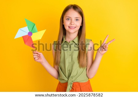 Photo of sweet blond little girl hold toy show v-sign wear khaki blouse isolated on yellow color background