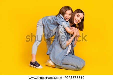 Photo of two relaxed fooling sisters wear jeans shirts smiling sitting floor embracing isolated yellow color background