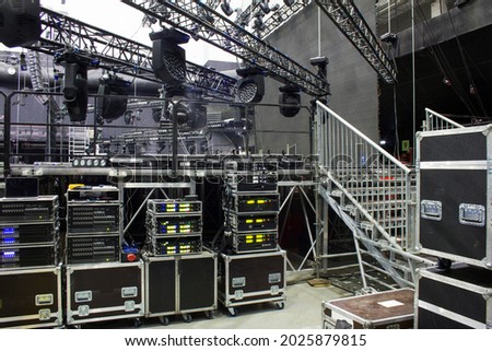 Installation of professional sound, light, video and stage equipment for a concert. Backstage area and tech zone with amplifiers, flight cases and radio microphones. Royalty-Free Stock Photo #2025879815