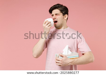 Sick unhealthy ill allergic man has red watery eyes runny stuffy sore nose suffer from allergy trigger symptoms hay fever hold paper napkin handkerchief isolated on pastel pink color background studio Royalty-Free Stock Photo #2025880277