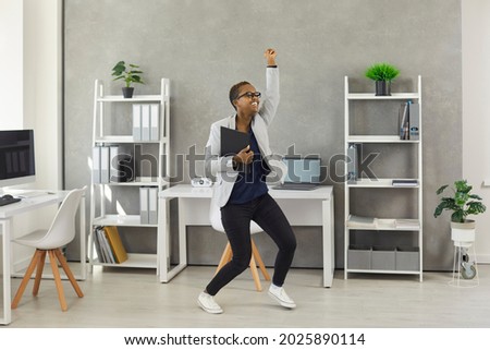 Excited carefree business woman holding office papers, dancing and having fun during break at work.Funny happy modern short haired active young girl feeling free from responsibility as vacation starts Royalty-Free Stock Photo #2025890114