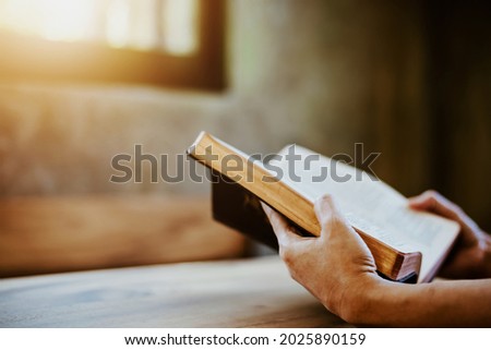 A woman holding and read book on wood table with window  light, crisis solution pray to God, Christian believe, trust and obey , morning devotional concept with copy space Royalty-Free Stock Photo #2025890159