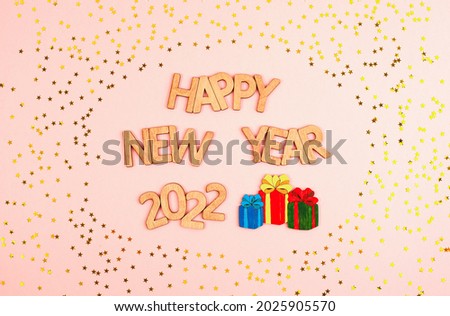 Colorful Christmas gifts and the inscription happy new year 2022 in wooden letters on a pink background surrounded by yellow stars. Beautiful Christmas card.