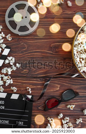 composition with film strip, clapperboard and popcorn on wooden background. festive bokeh. copy space. selective focus