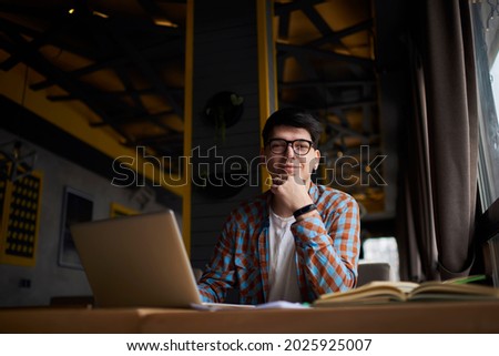Young millennial male sitting at table front open laptop computer while studying online. Modern digital nomad work on freelance on netbook in coffee shop interior