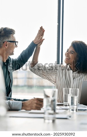 Two happy multiracial professional executive businessman and businesswoman colleagues giving highfive after victory of corporation project together at boardroom meeting. High five concept. Vertical. Royalty-Free Stock Photo #2025930392