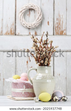 Easter table decoration with bunch of catkins and painted eggs in pink dotted can, on wooden table. 