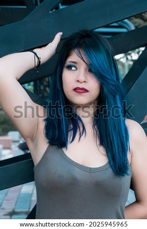young woman with blue hair standing by the bus stop. with a serious expression looking to the left. girl posing standing with hand to the side of her head and serious face