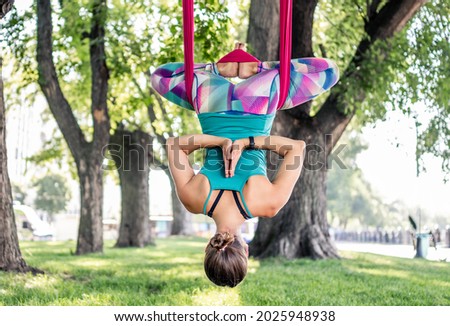 Sport girl practicing fly yoga in hammock at nature and stretching her body. Athlete woman during aero gymnastics outdoors