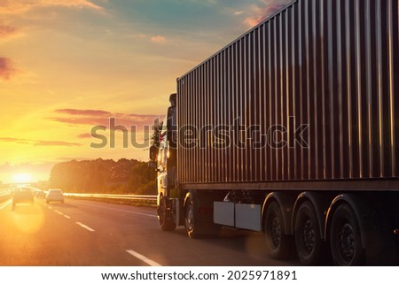 Scenic front view big long heavy semi-treailer truck with sea shipping container driving highway dramatic warm morning evening sunrise sun sky sunset. Cargo transport industry background concept Royalty-Free Stock Photo #2025971891