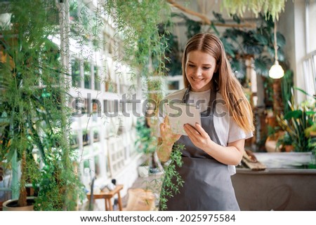 A female florist entrepreneur works in her workshop. Flowers and various exotic plants for sale. Surf the Internet for information about plants. In a form for convenient operation.