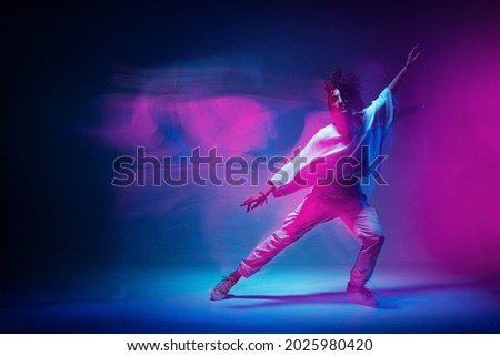 Colourful shot of dancing girl. Female dancer performer show expressive hip hop dance. Colored neon light, long exposure Royalty-Free Stock Photo #2025980420