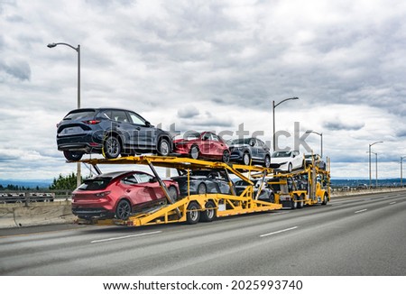 Professional powerful yellow big rig industrial car hauler semi truck with two level modular hydraulic semi trailer transporting cars moving on the wide multiline highway road with stormy sky Royalty-Free Stock Photo #2025993740
