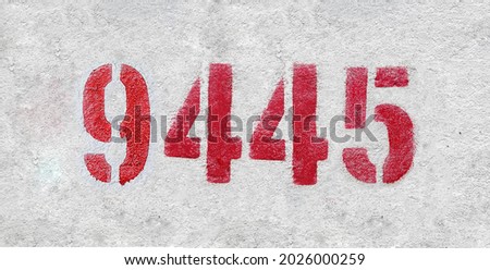 Red Number 9445 on the white wall. Spray paint. Number nine thousand four hundred and forty five.