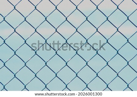 Pattern of metal net fence in front of a blue sky.