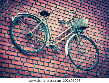 Old rusty bike attached to red brick wall. Aged photo.