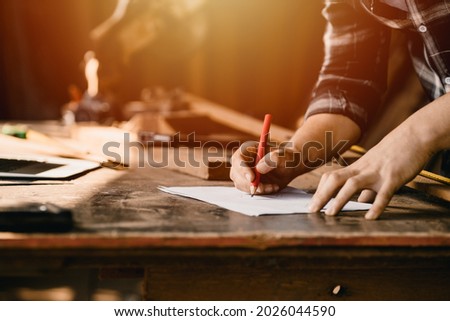 closeup male worker hand using pencil to sketch drawing draft design wooden workpiece in DIY workshop. Royalty-Free Stock Photo #2026044590