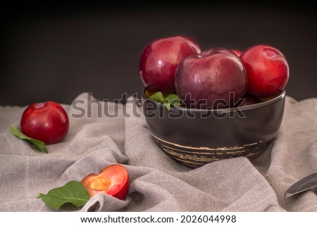 Still life with large black plums in a deep plate.