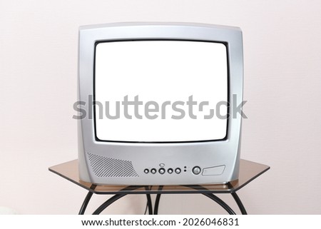A retro TV with a white screen for adding images stands on a table in a room against a background of vintage wallpaper. 