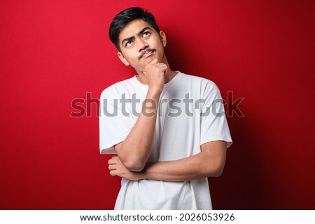 Young handsome man wearing white t-shirt standing over red background Thinking worried about a question, concerned and nervous with hand on chin