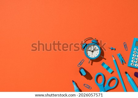 Top view photo of blue school supplies stationery calculator markers pencil clips pushpins scissors and alarm clock on isolated orange background with empty space
